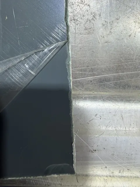 Anthrazit lackiertes Blech mit Schutzfolie, an der Kante abgesplitterter Lack